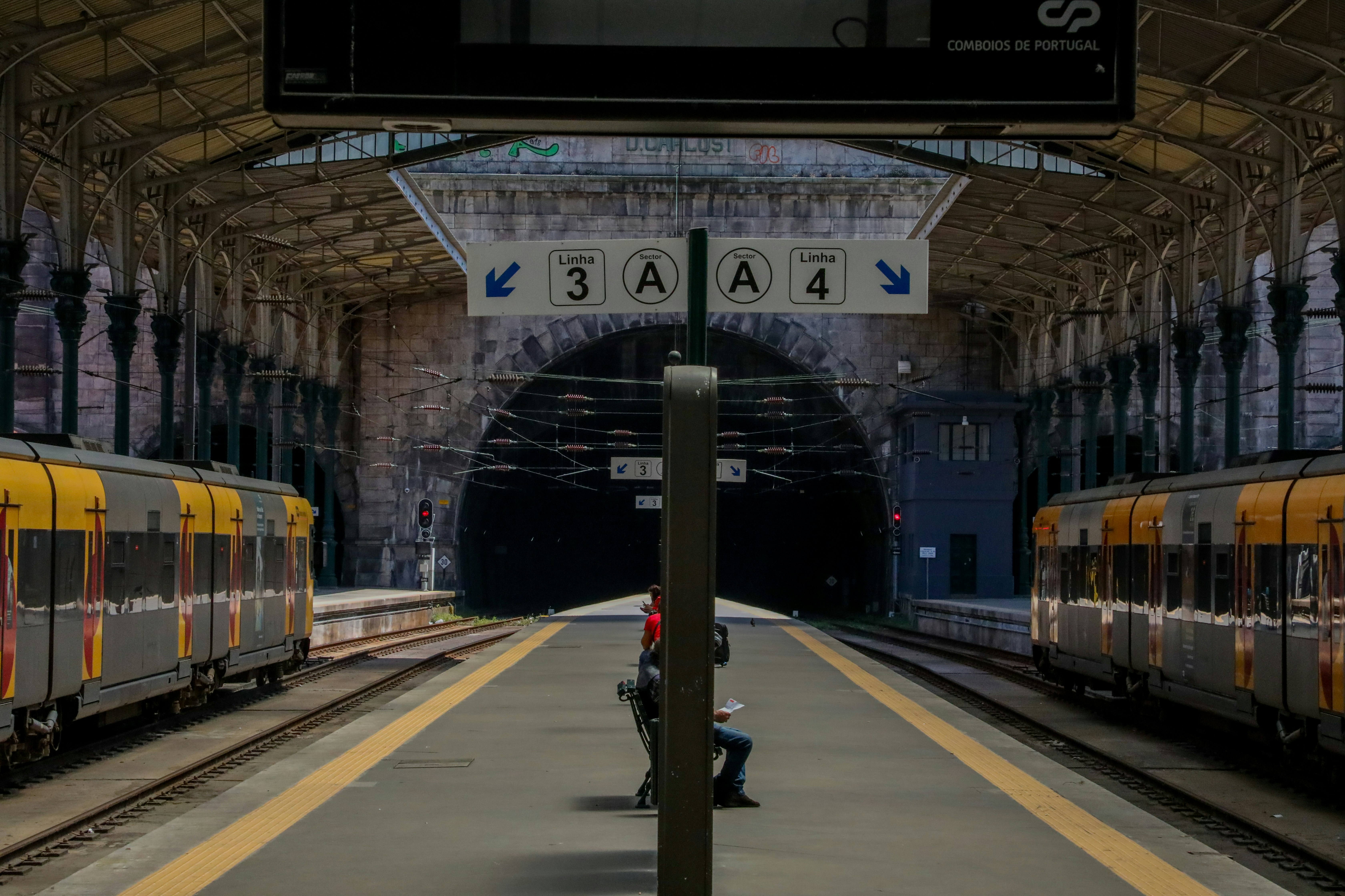 several people sitting on bench in between two passing trains at train station